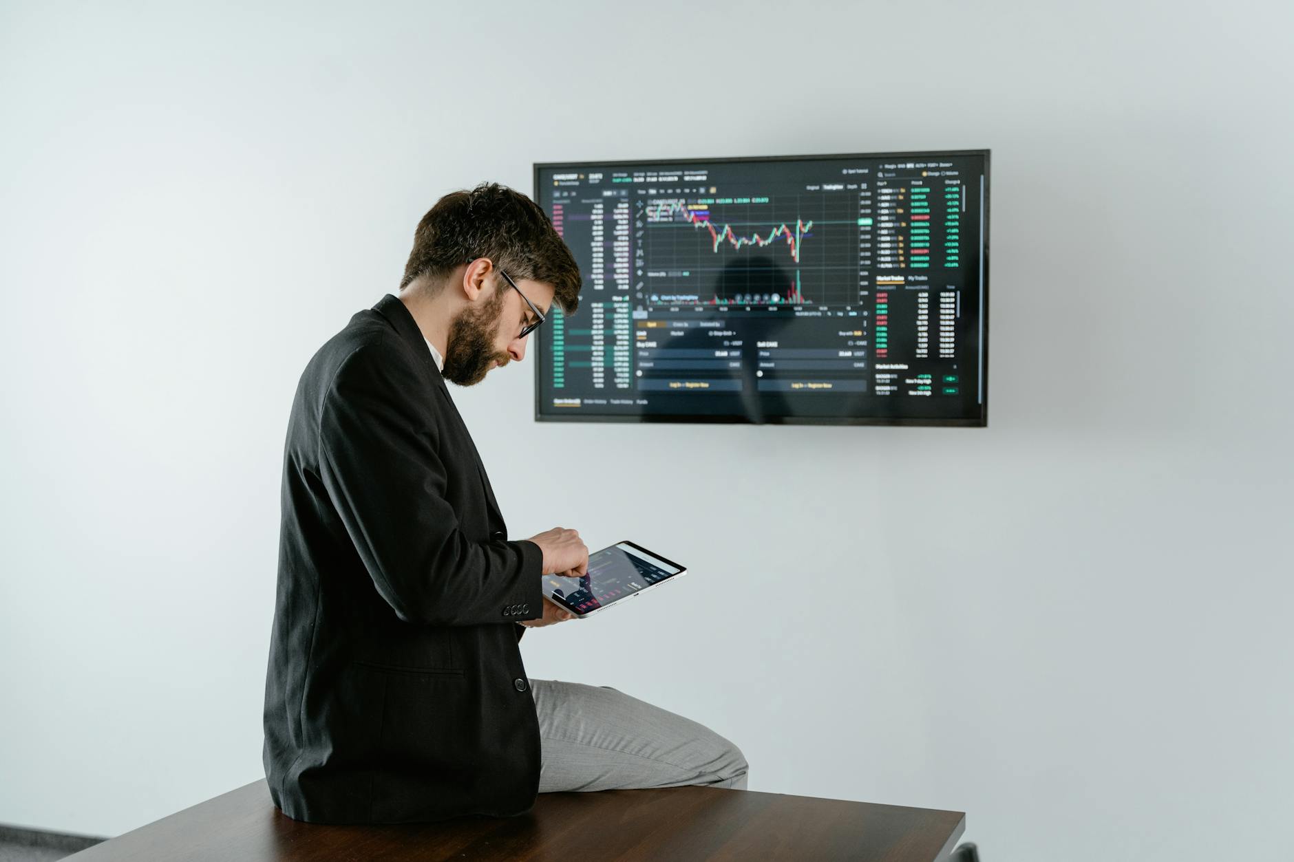 Young analyst examining financial graphs on a tablet with stock market screen displays