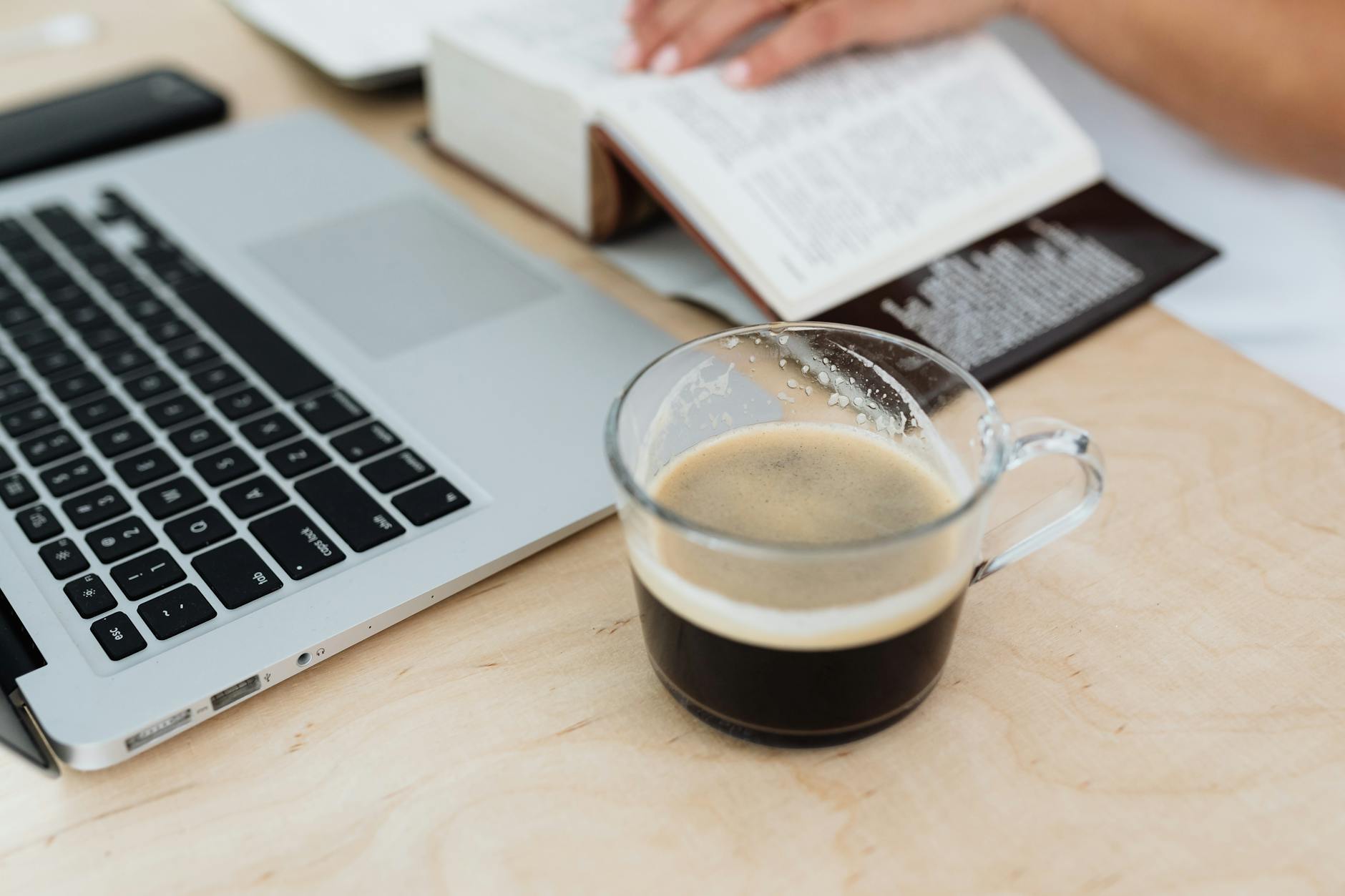Cozy workspace setup with a laptop, book, and coffee cup on a wooden desk
