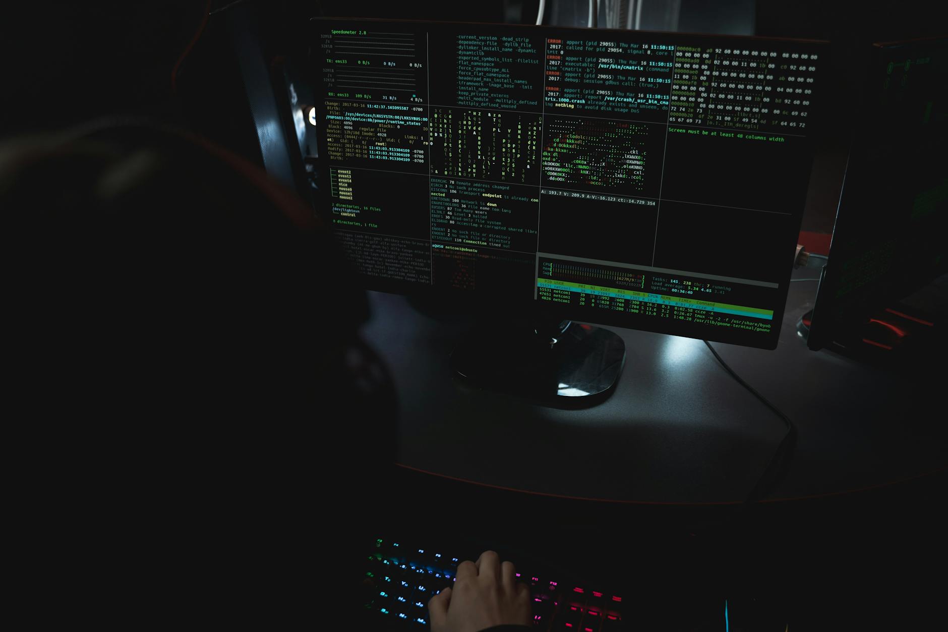 Dark room setup with code displayed on PC monitors highlighting cybersecurity themes