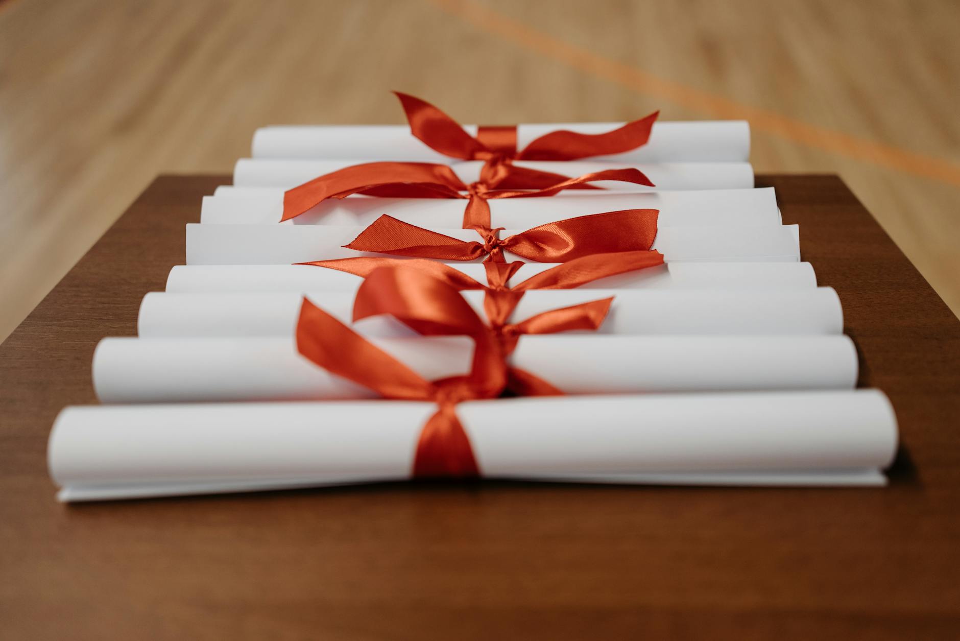 Close-up of rolled diplomas tied with red ribbons on a wooden desk