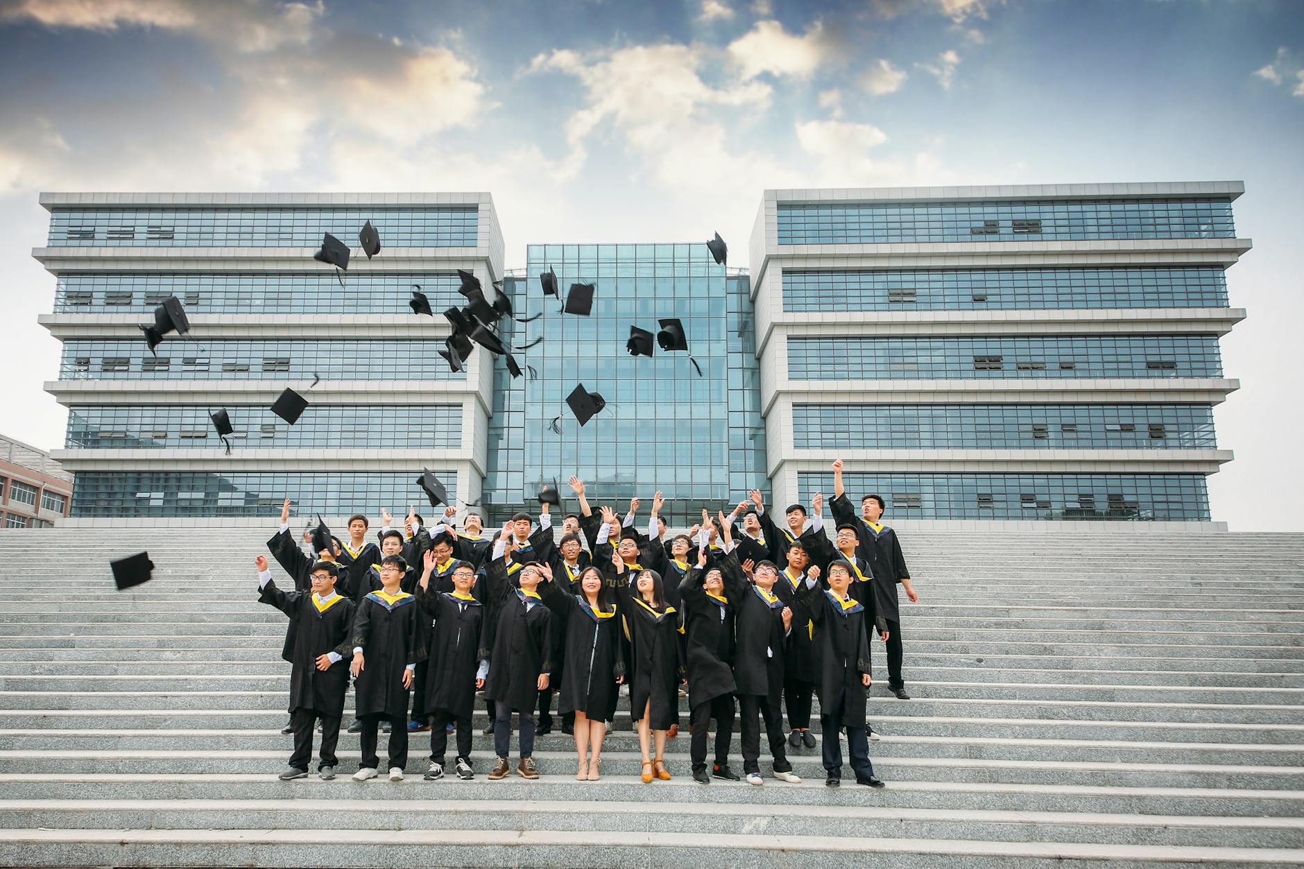 Group of graduates celebrating and tossing caps outside a modern building