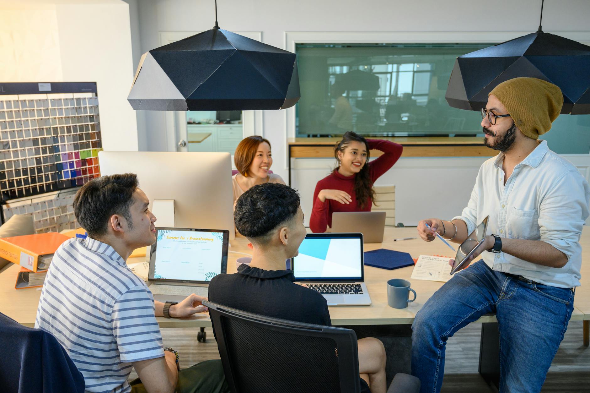 Diverse team discussing ideas around a table in a modern office with laptops and tablets