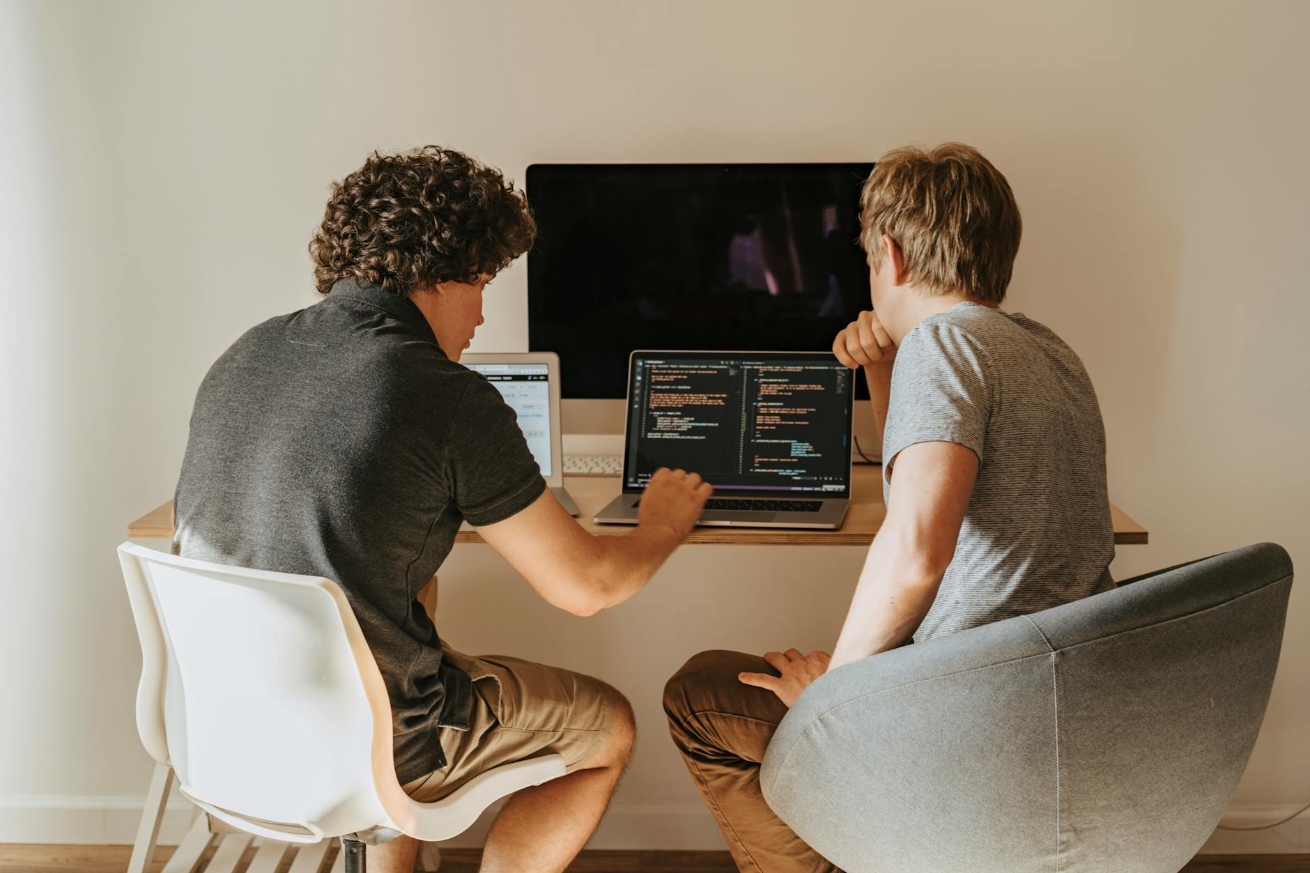 Two developers working on laptops indoors, discussing code