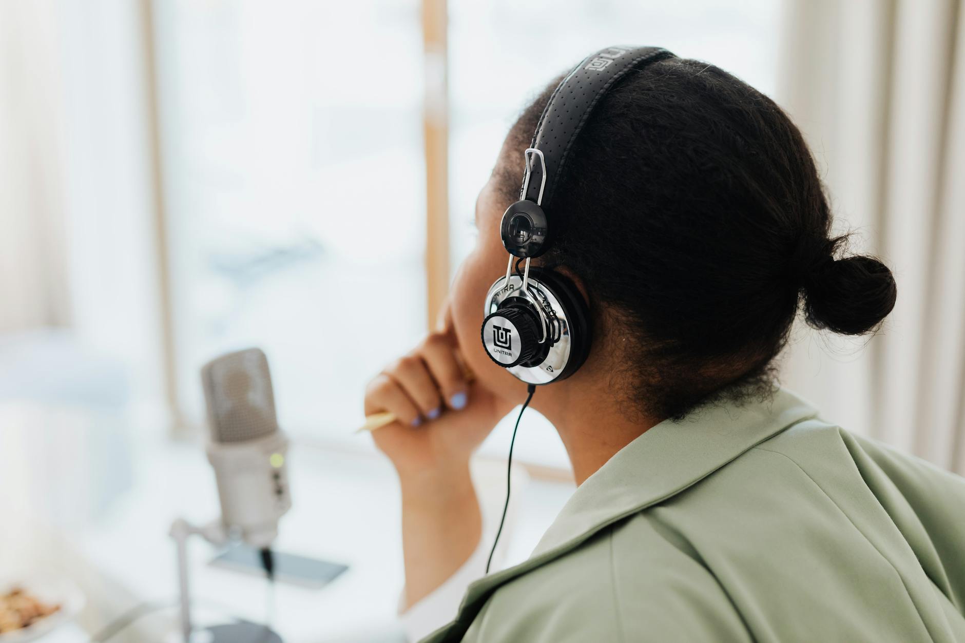 A woman wearing headphones engaged in podcasting indoors by a window