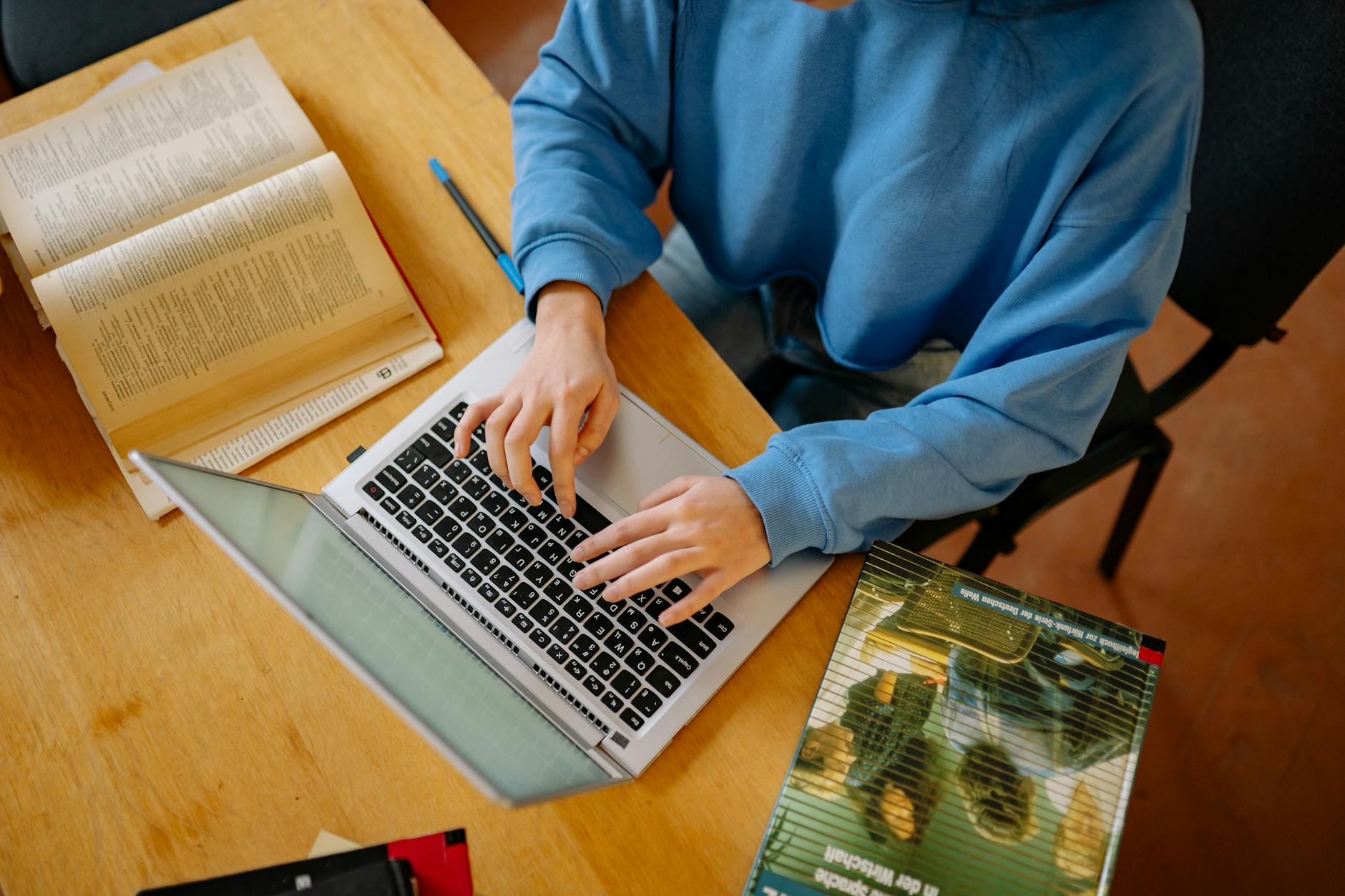 A student typing on a laptop surrounded by open books, focusing on research