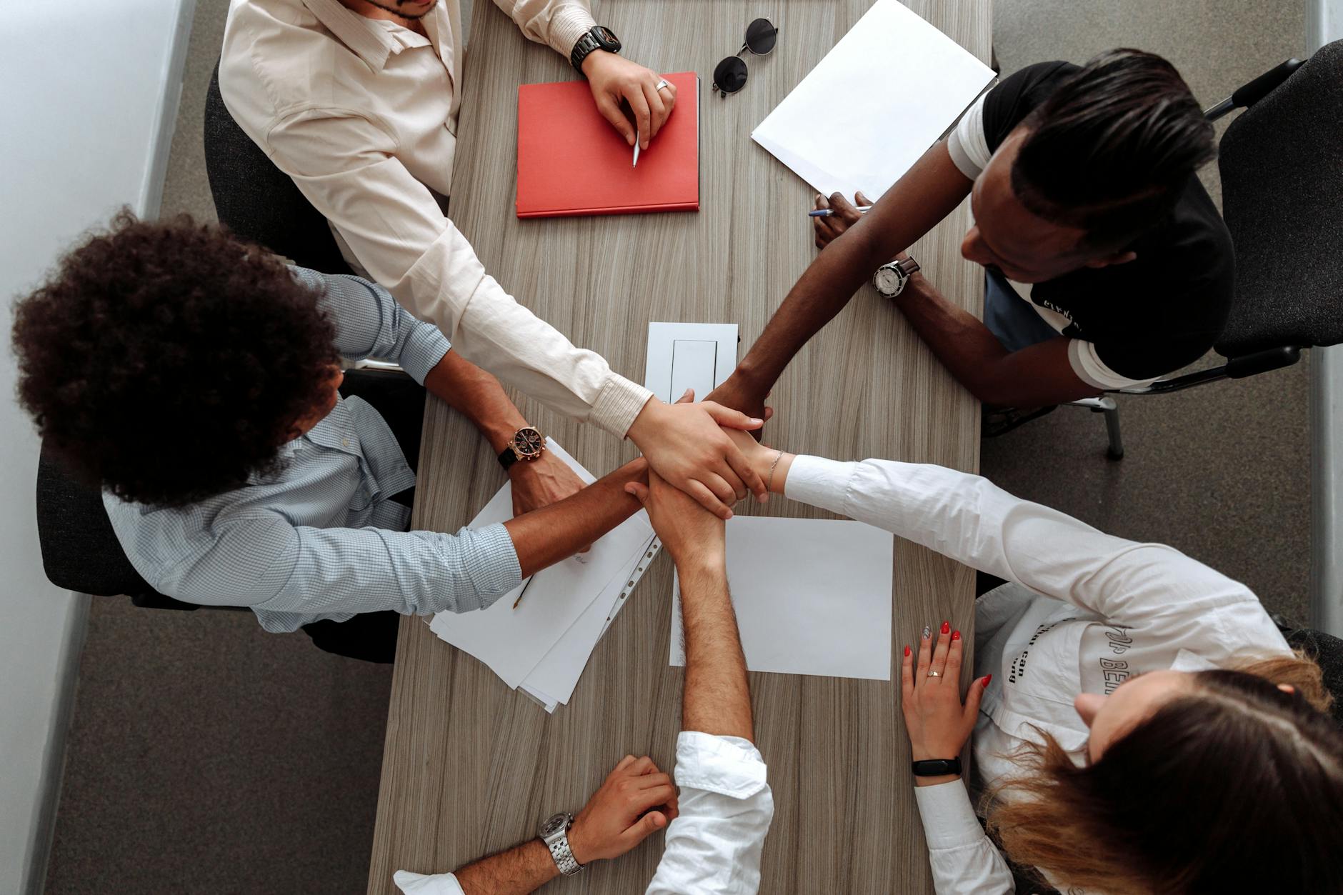 Overhead view of a diverse team placing hands together in a sign of unity during a meeting