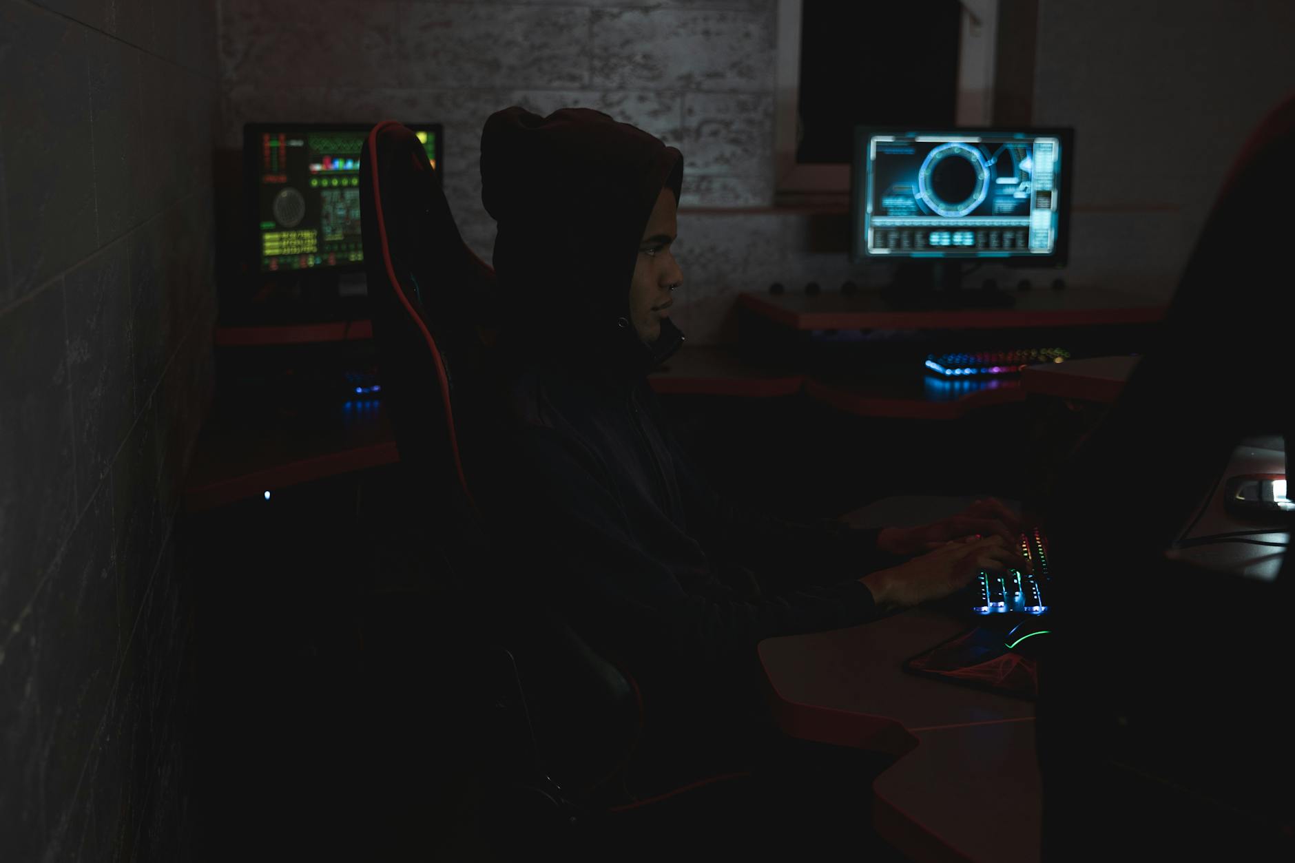 A professional analyzing data on multiple monitors in a dark room, highlighting cybersecurity themes