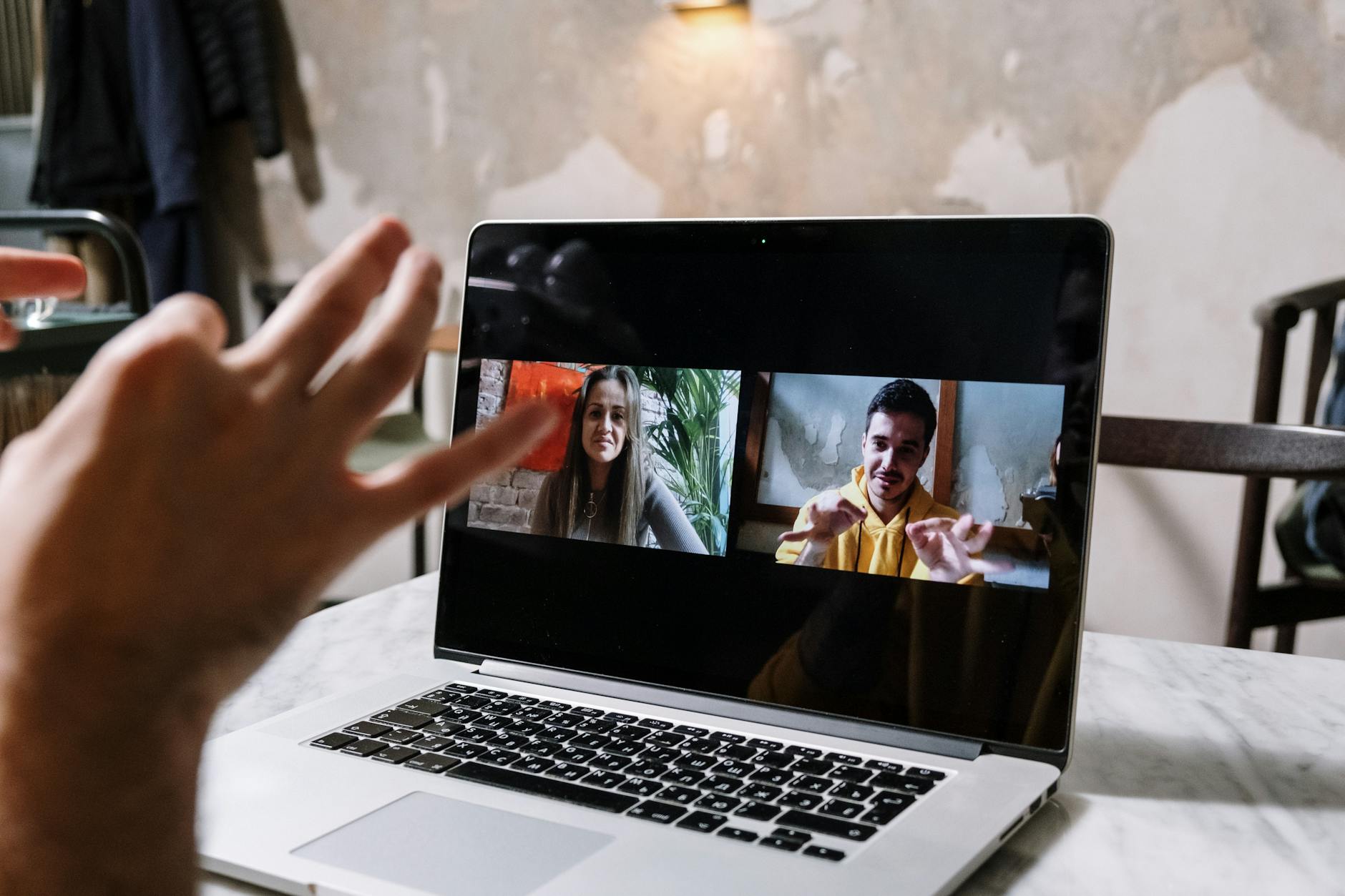 Hands gesturing during a video call on a laptop screen, showing two people in a virtual meeting